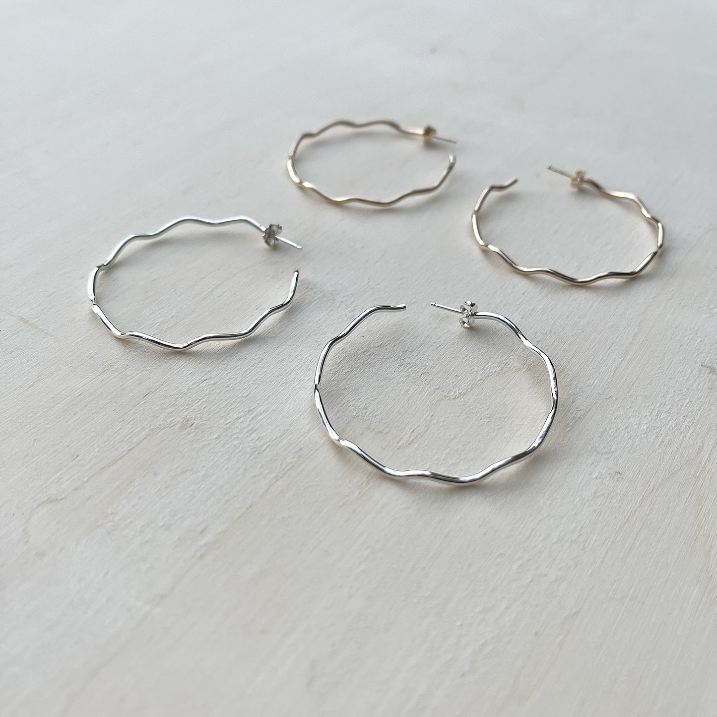 Set of silver and gold hoop earrings on a light wooden surface