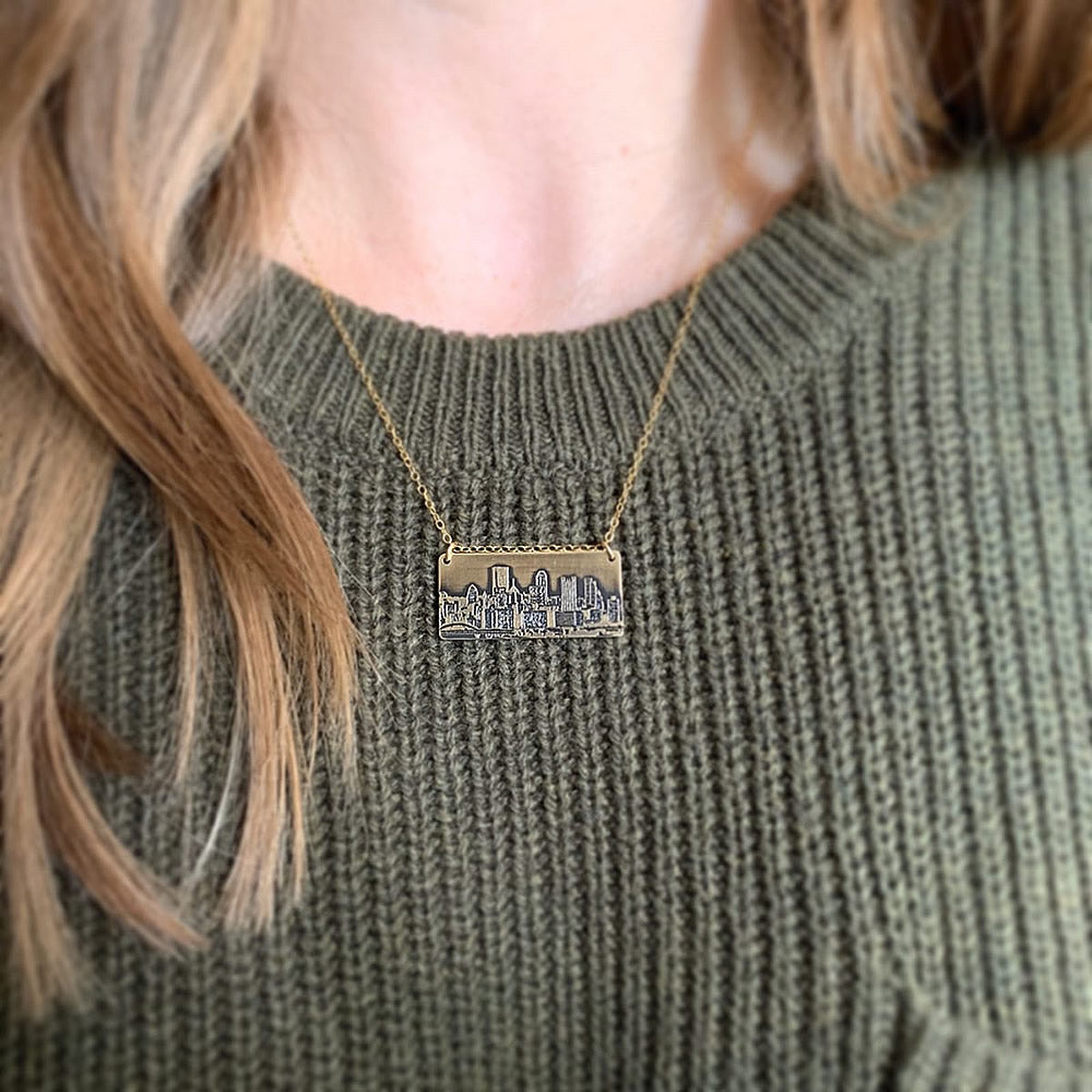 brass pittsburgh skyline pendant worn on person with green sweater handmade jaci riley jewelry