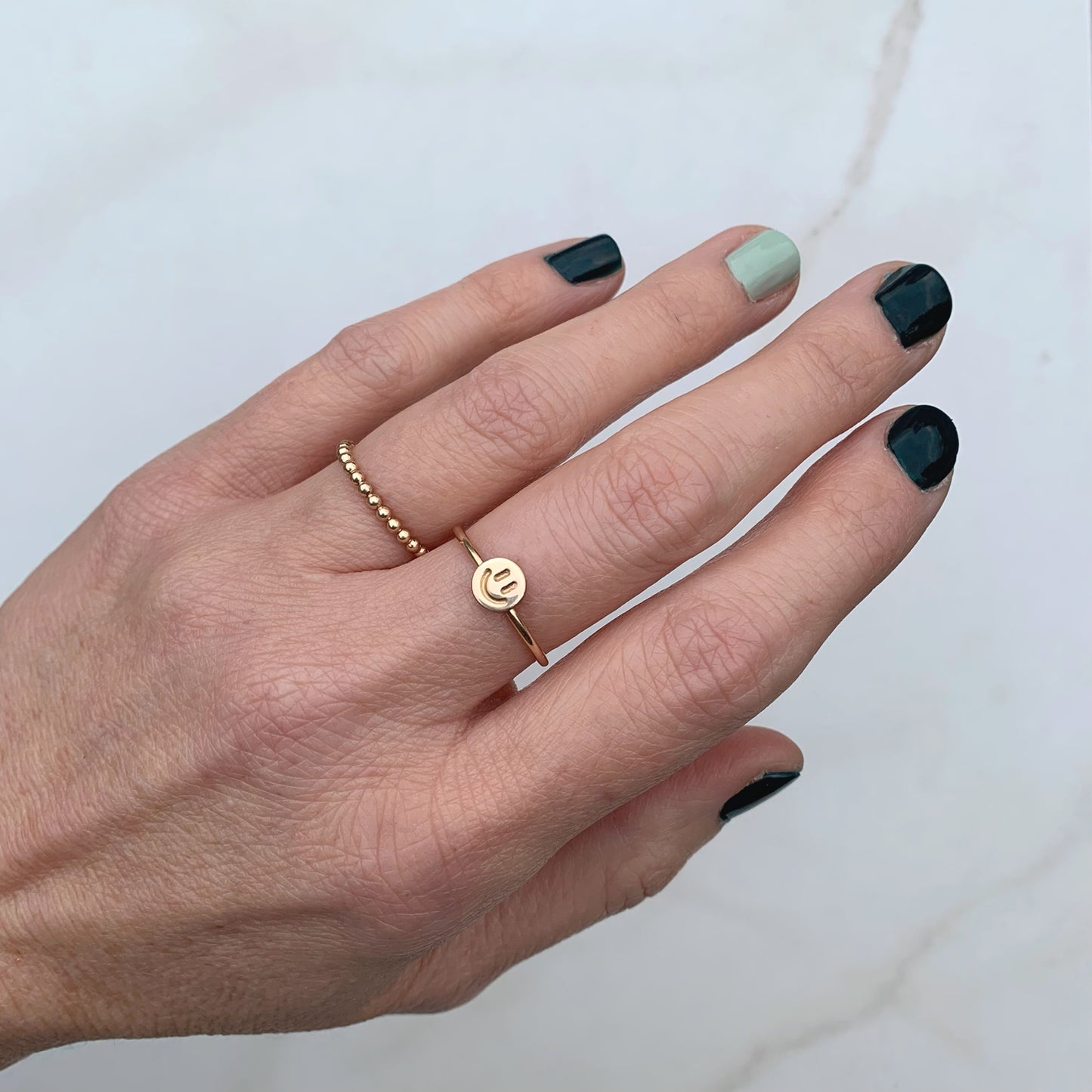 gold smiley face ring and gold beaded ring modeled on a hand