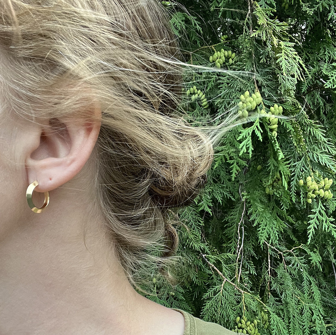 gold hoop earrings in a person's ear with a tree in the background