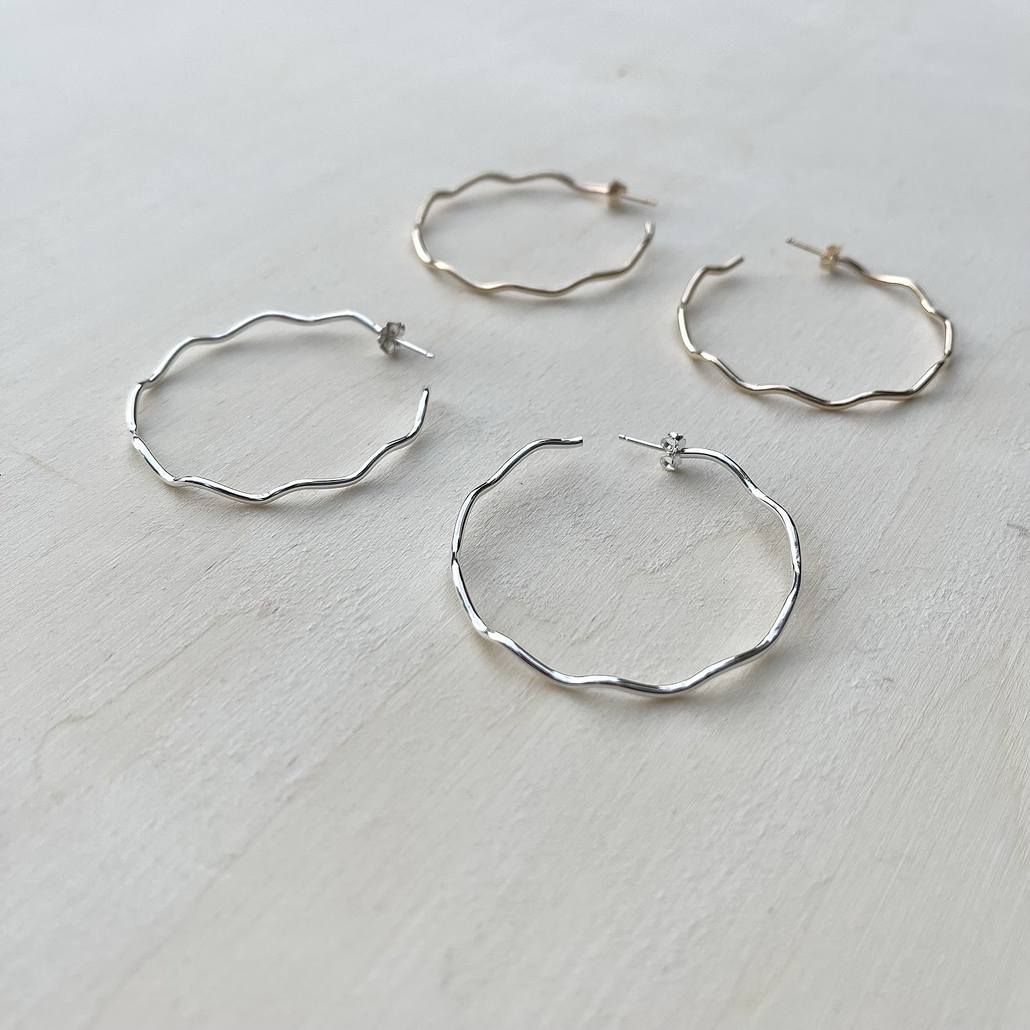 Set of silver and gold hoop earrings on a light wooden surface