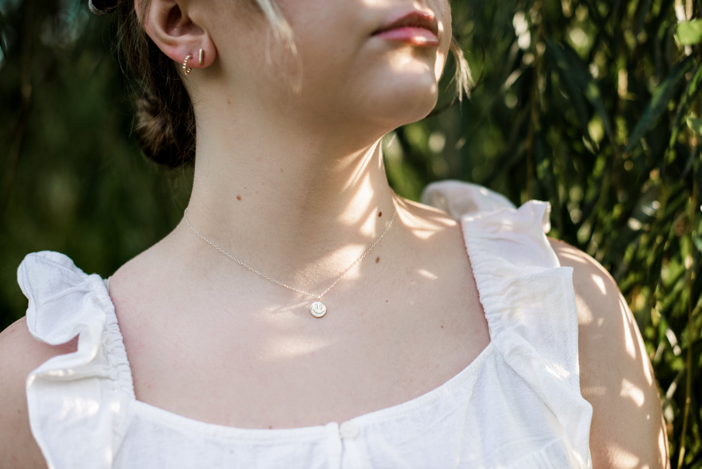 gold smiley face necklace on a model with a white shirt