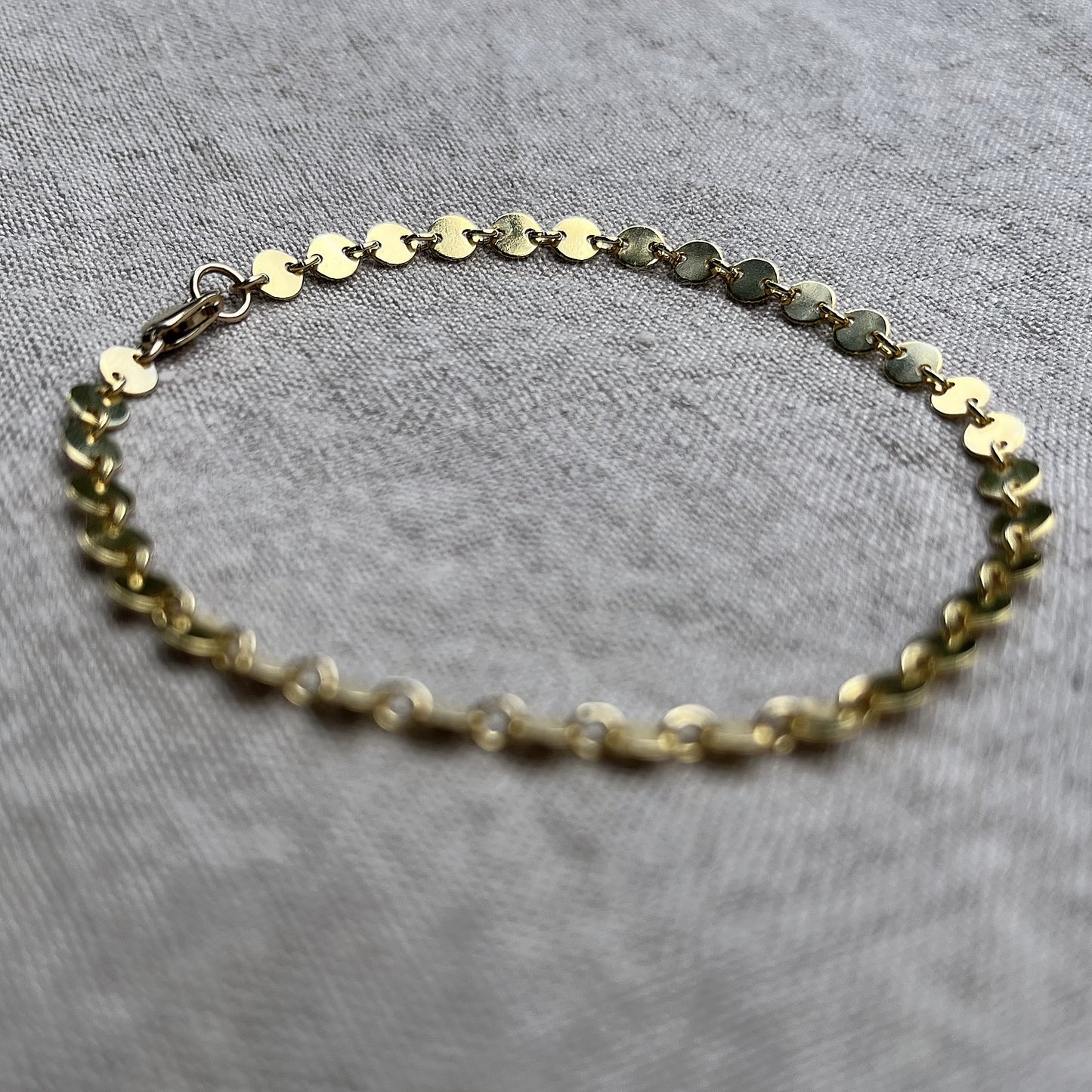 14k gold filled coin chain bracelet on a linen background