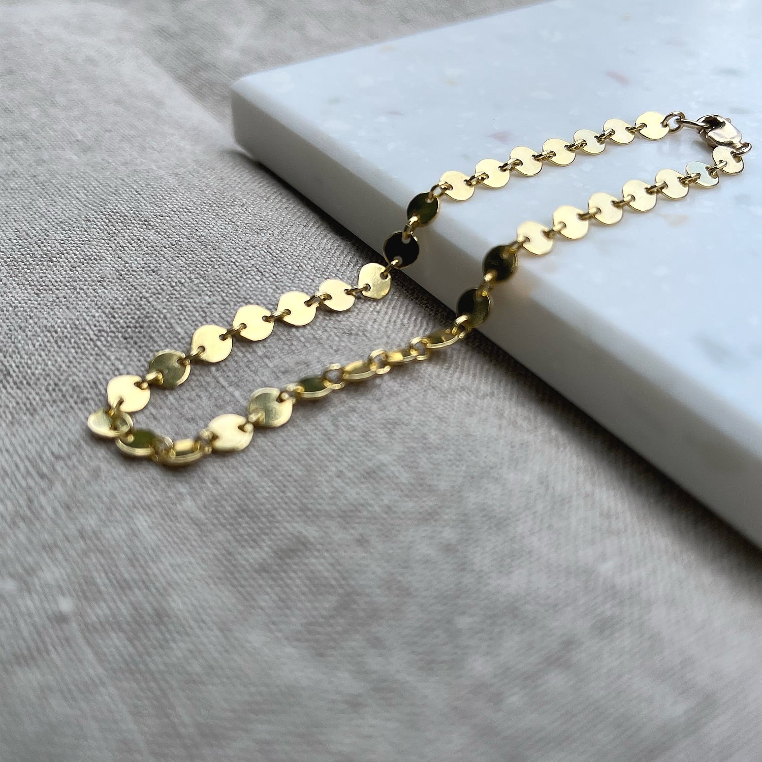 14k gold fill coin chain bracelet on a tile with a linen background