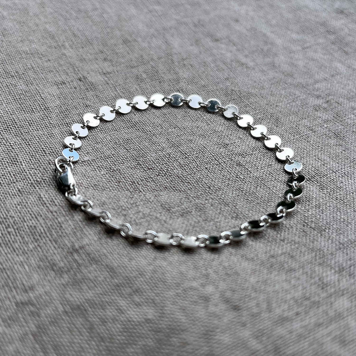 sterling silver coin chain bracelet on a linen background
