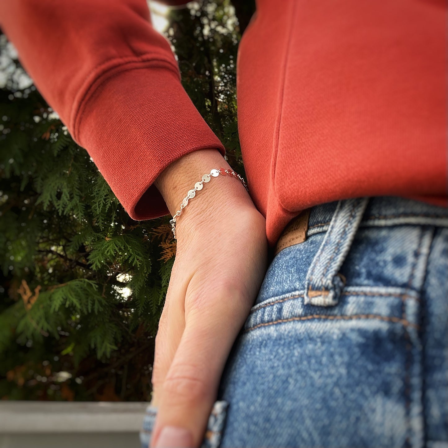 sterling silver coin chain bracelet on a person with a red sweatshirt and blue jeans