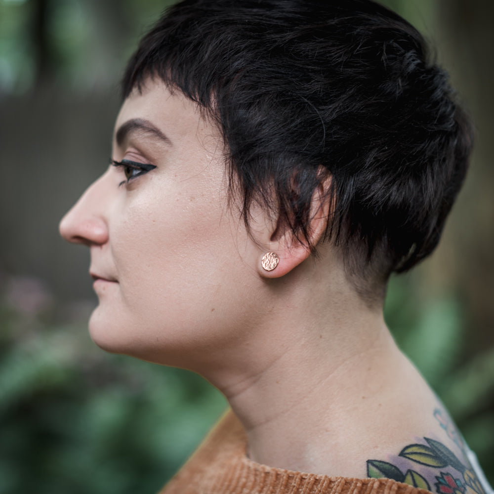 hammered stud earrings in copper on model with short hair and tattoos