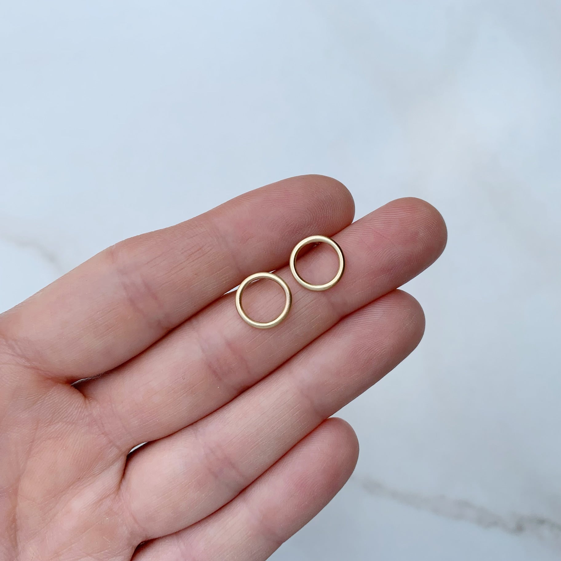open circle studs in brass, held in a hand