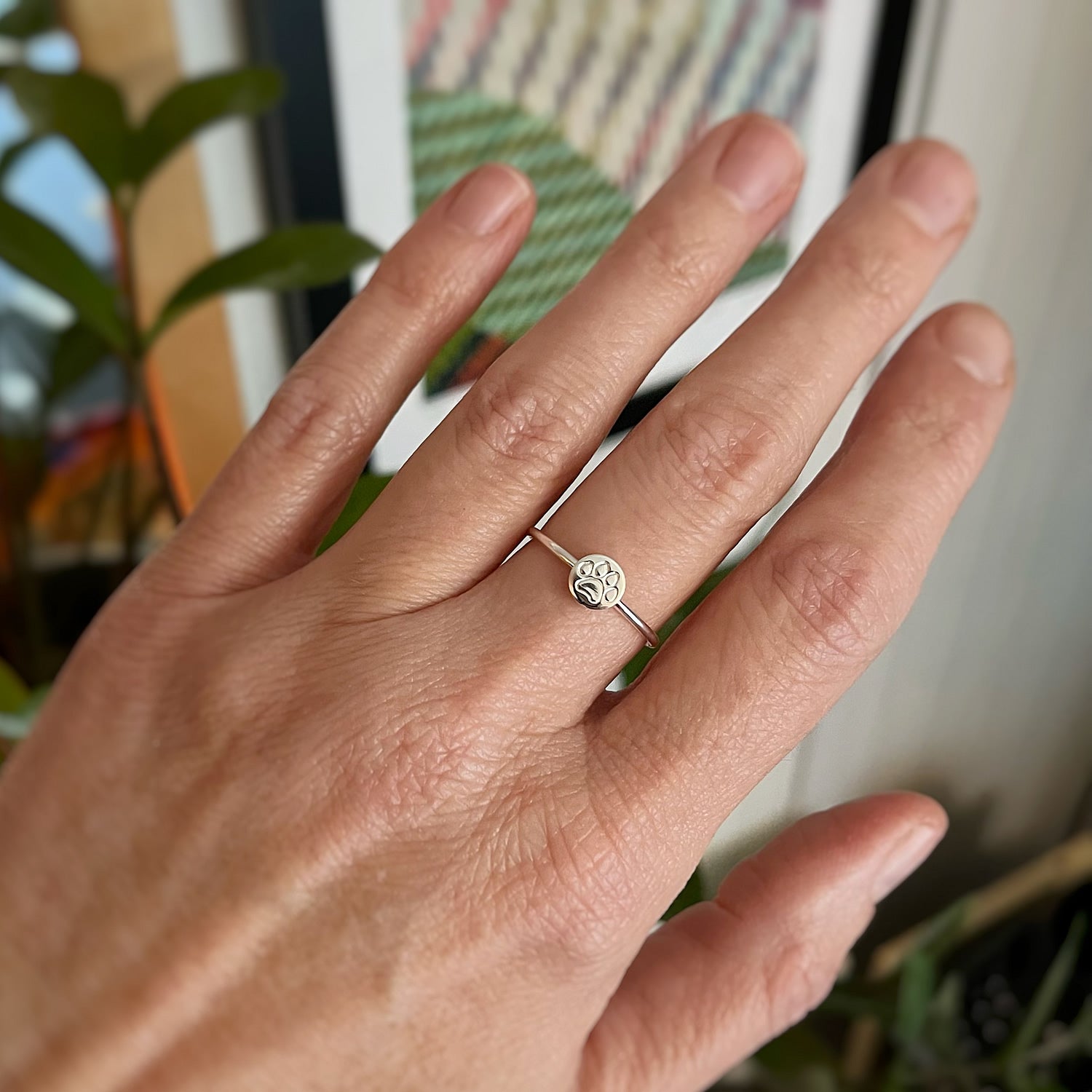 sterling silver paw print ring on a hand with art by natalie lanese in the background