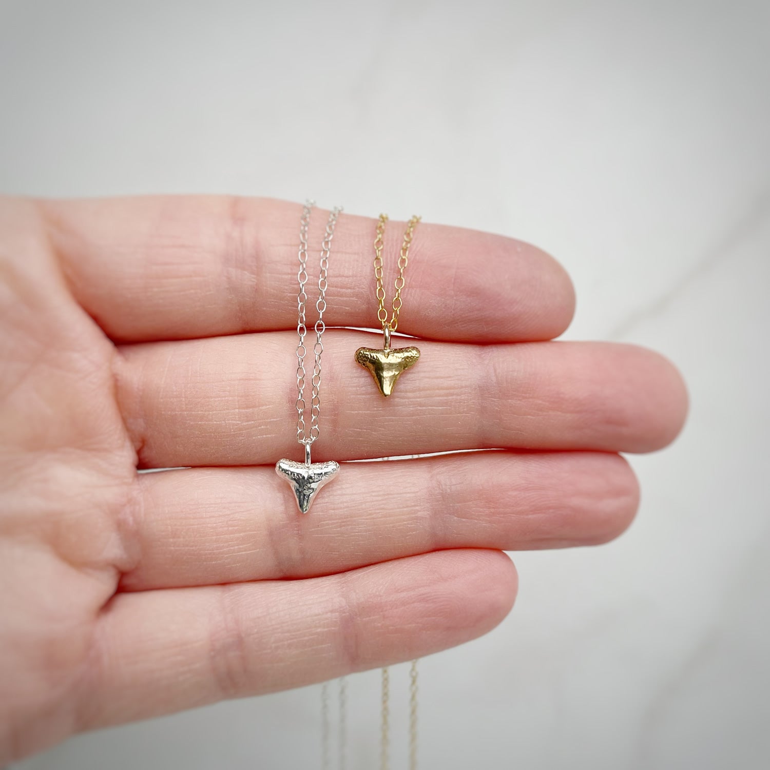 sterling silver and gold vermeil shark tooth necklaces in a person's hand with a white background