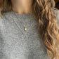 gold smile necklace on a person with a gray sweater