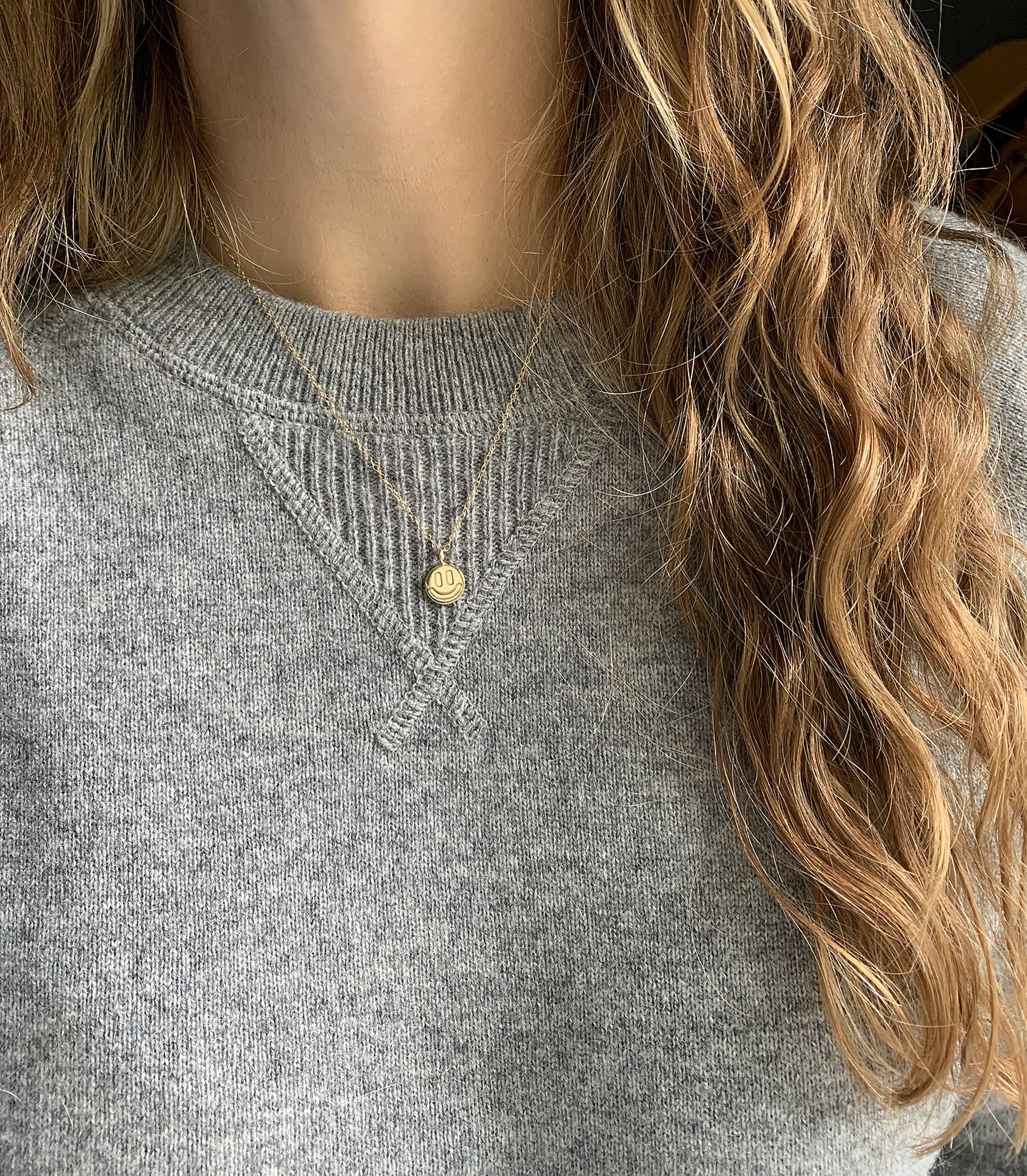 gold smile necklace on a person with a gray sweater