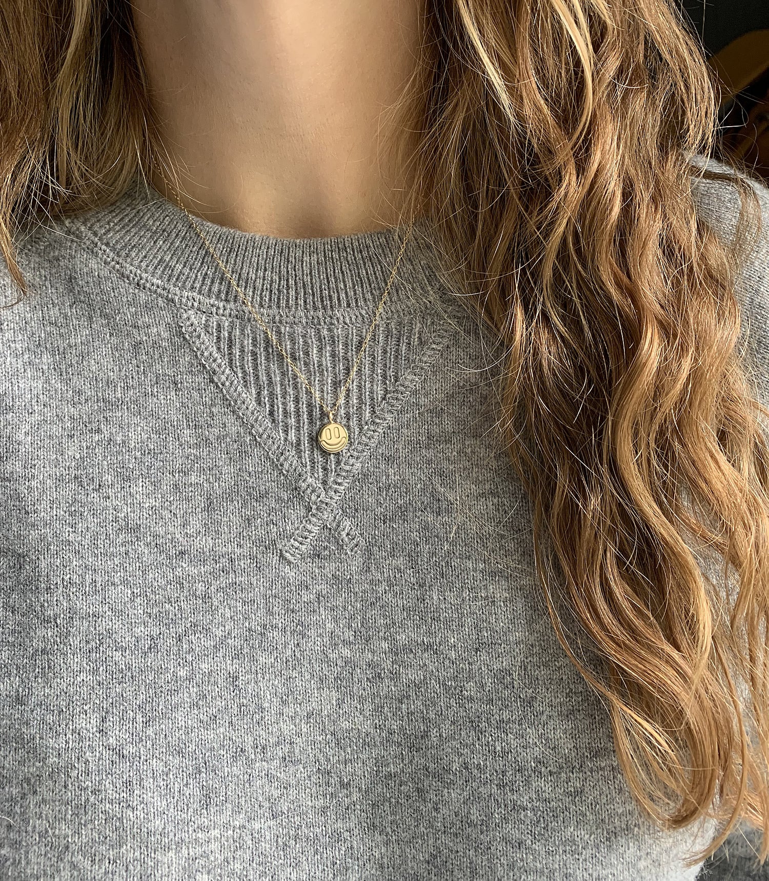 gold smile necklace on a person with a gray sweater